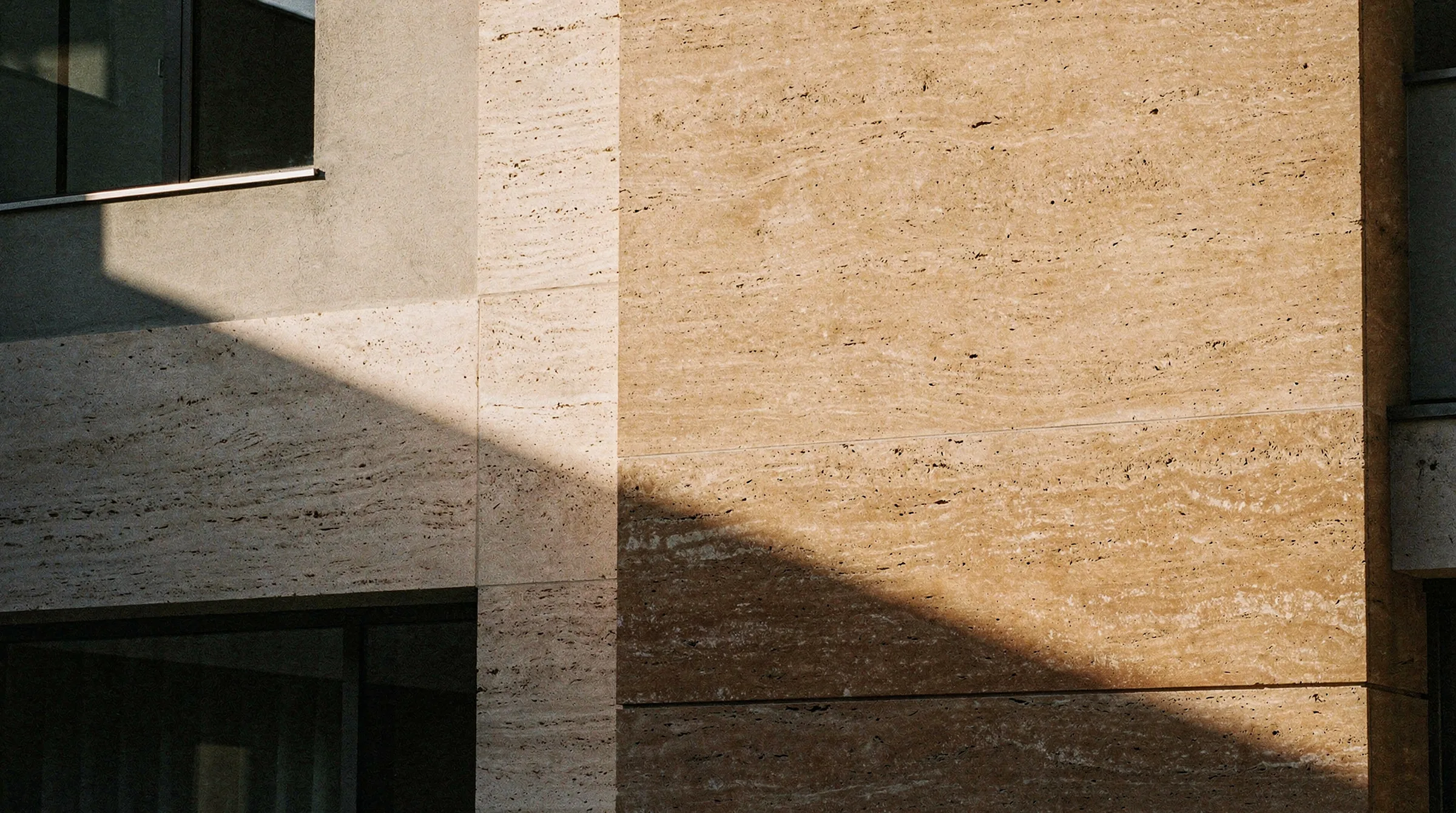 Late-afternoon sun cutting a hard diagonal shadow across a travertine facade